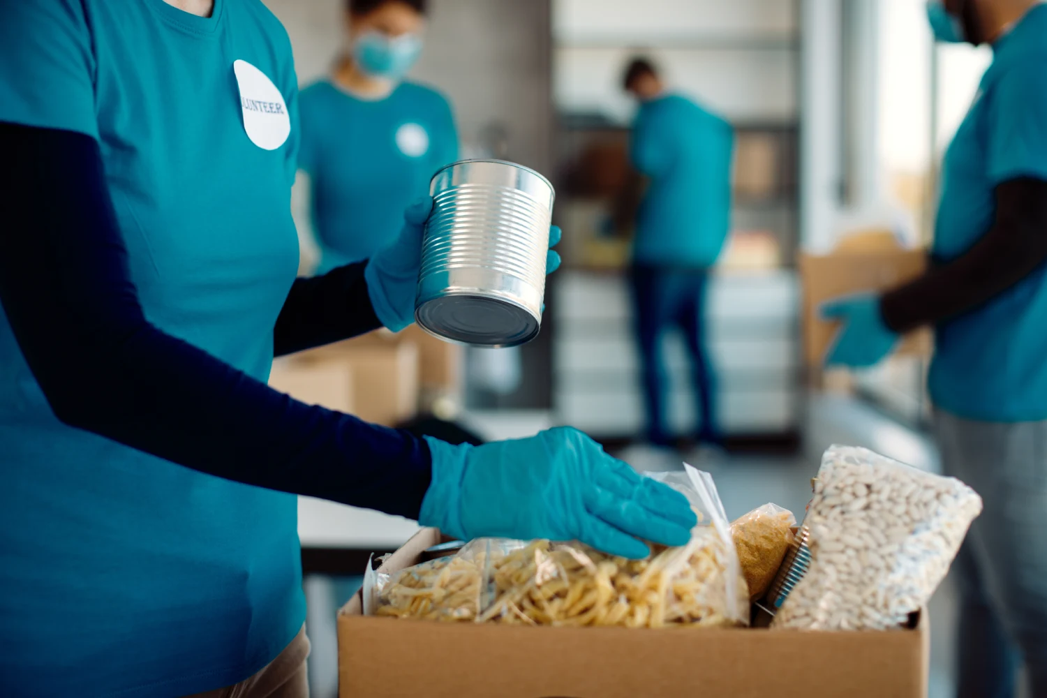 Volunteers in blue shirts and gloves pack canned goods and dried foods into boxes.