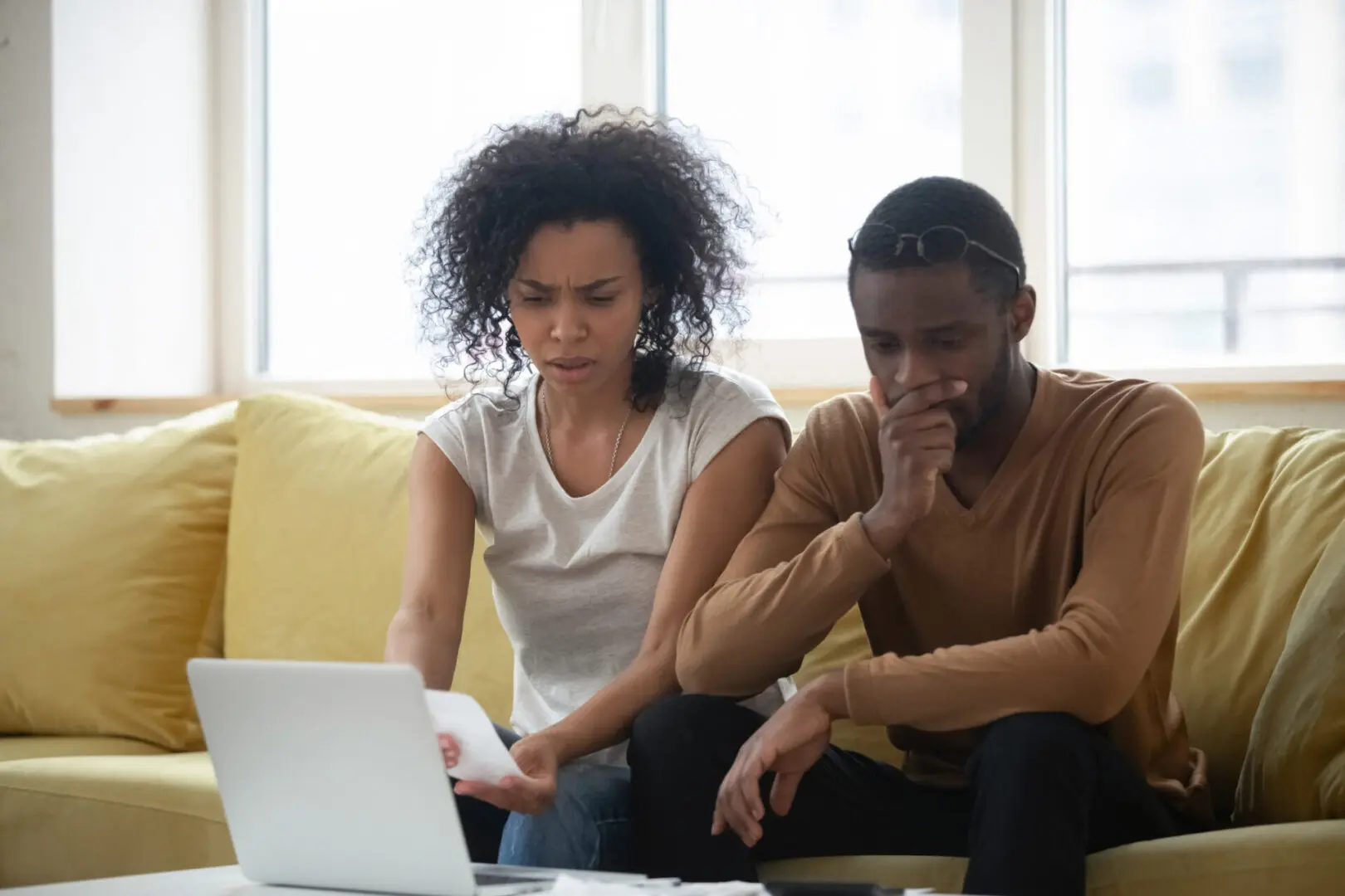 African spouses sitting on couch at home planning budget using laptop application check bills cheques feels troubled by overspending, American couple manage family expenses financial problems concept