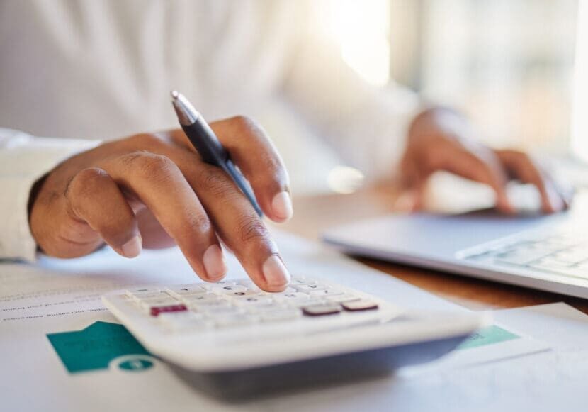 Person using calculator beside laptop and documents.